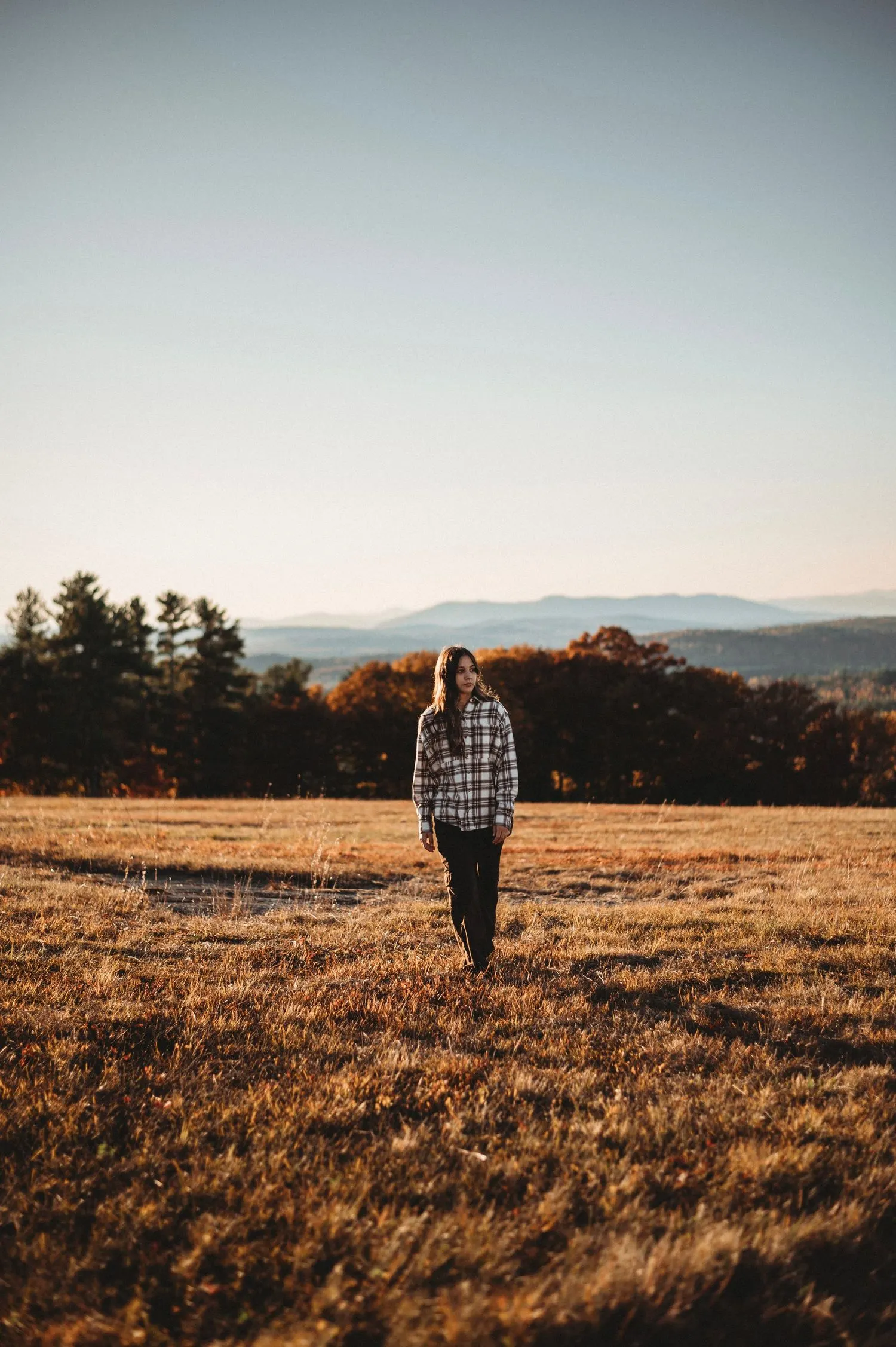 Senior portrait of a high school girl walking through a field with mountain views. Captured during golden hour by a photographer in Casco.
